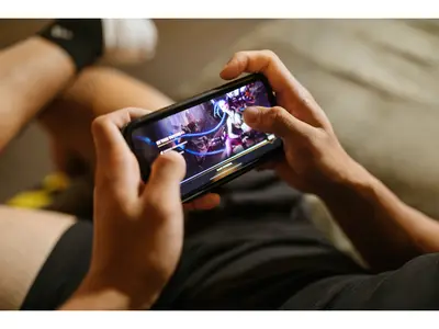 A person holding a smartphone with both hands while playing a colorful mobile game