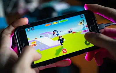 Hands holding a phone playing a Roblox-style blocky-avatar game on a bright green 3D course
